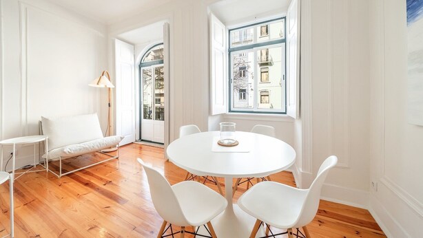 A room with a round white table, white chairs, a white sofa, and large windows with views of buildings. - GuestReady - Castle - Apt for 4 guests in Saldanha (Lisboa)