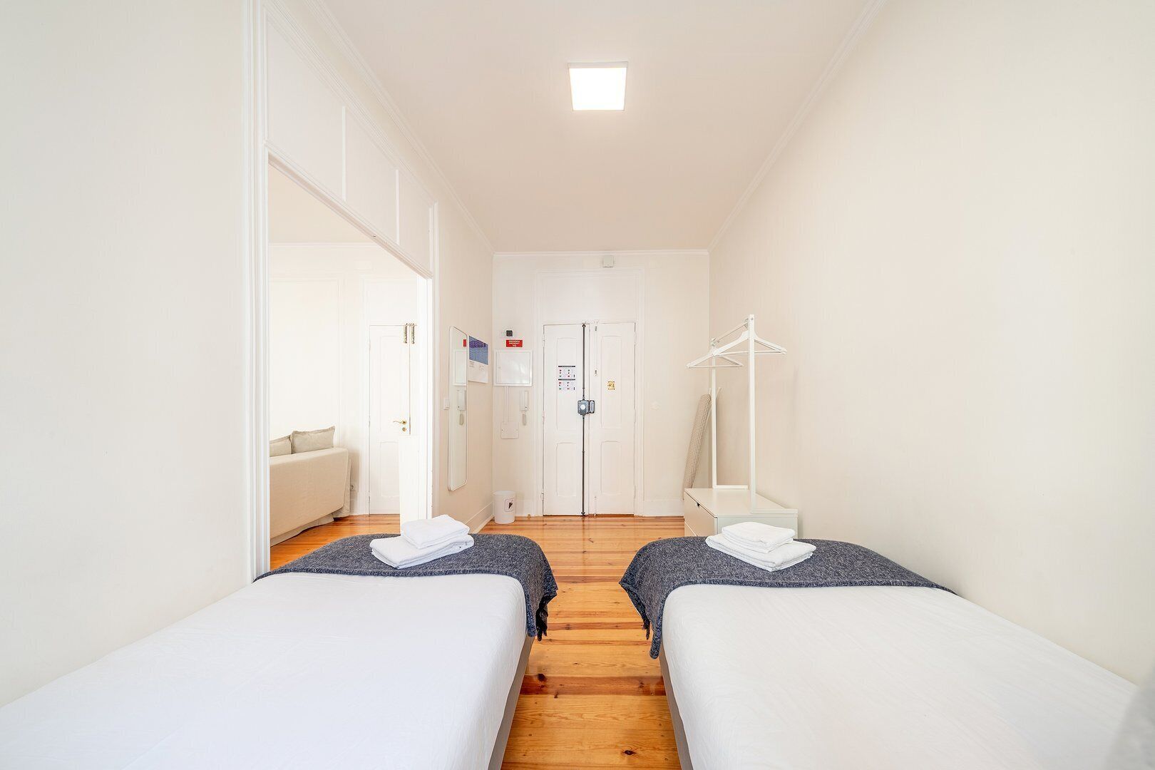 A hotel room with two beds, a sofa, a coat rack, and a door with a mirror.
