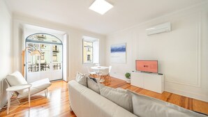 A modern living room with a sofa, a dining table with chairs, a TV, and a view of the outside. - GuestReady - Castle - Apt for 4 guests in Saldanha (Lisboa)