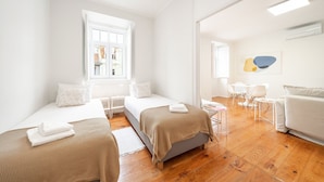 Une chambre d’hôtel avec deux lits simples, un coin salon avec une table et des chaises, une fenêtre donnant sur un paysage agréable et un climatiseur fixé au mur.