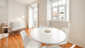 Une pièce avec une table ronde blanche, des chaises blanches, un canapé et une lampe.