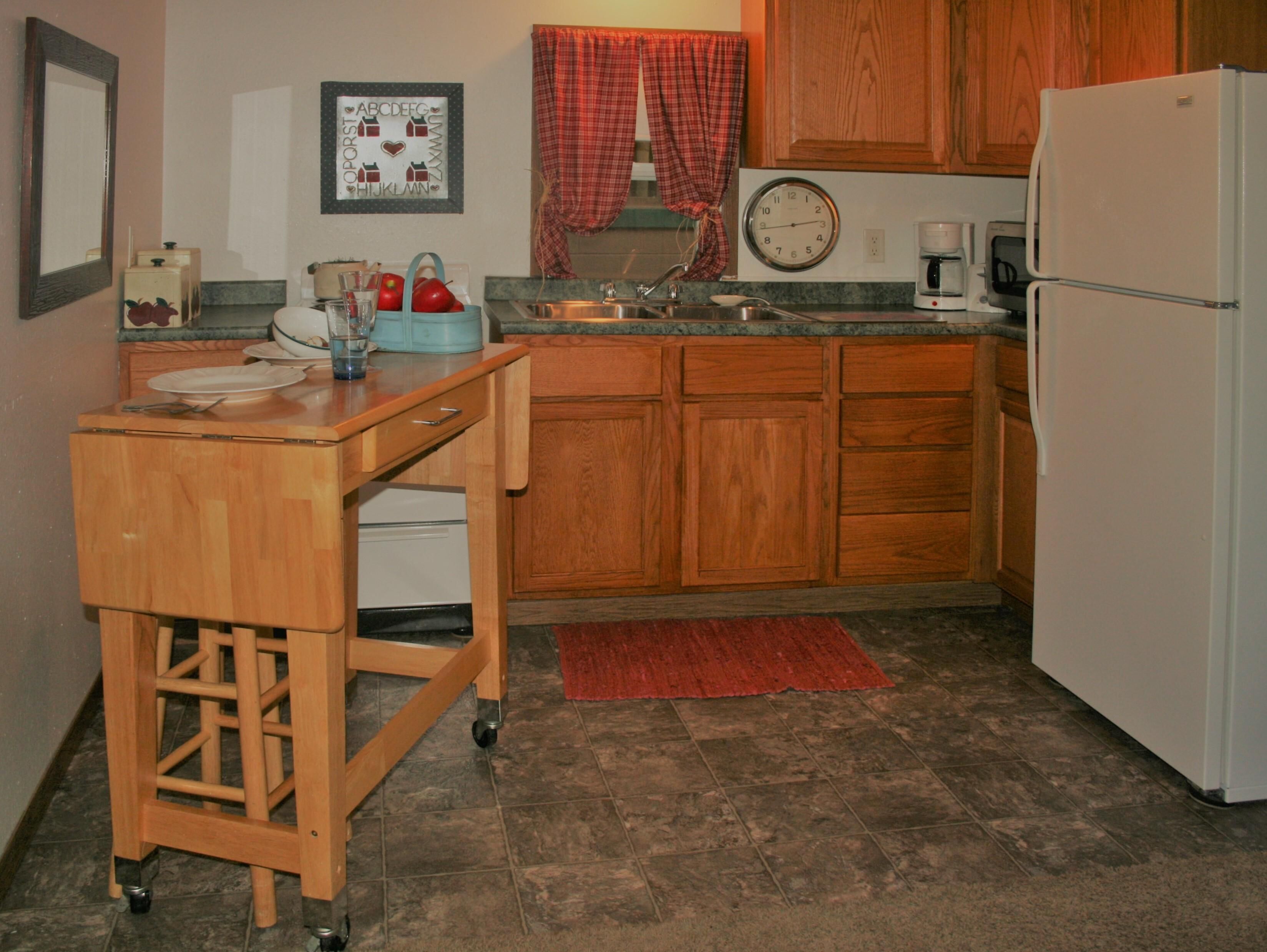 A compact kitchen with wooden cabinets, a sink, a clock, and a refrigerator.