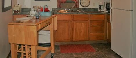 A compact kitchen with wooden cabinets, a sink, a clock, and a refrigerator.