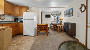 Cocina compacta con armarios de madera, un refrigerador blanco y un comedor con mesa y sillas.