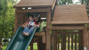 A wooden play structure with a slide, including a platform and a covered area.