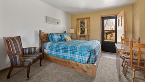A bedroom with a wooden bed, a striped chair, a wooden table, and a door leading outside.