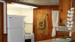 Une cuisine avec des meubles de rangement en bois, un réfrigérateur blanc, une cuisinière et une chaise verte.