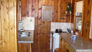 Une petite cuisine aux murs en bois, avec un évier, une cuisinière et des tabourets.