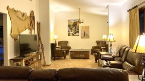A living room with leather sofas, a coffee table, and a TV. There are paintings on the wall and a fur rug. - Cougar Lodge Vacation Home Thirty Minutes from Mt Rushmore - In Rapid City On Canyon Lake Thirty Minutes from Mt Rushmore (Rapid City)