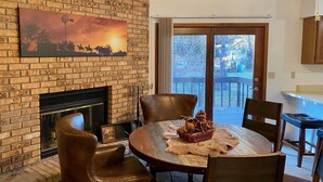 A cozy dining area with a brick fireplace, leather chairs, and a table set with a rustic centerpiece. - Cougar Lodge Vacation Home Thirty Minutes from Mt Rushmore - In Rapid City On Canyon Lake Thirty Minutes from Mt Rushmore (Rapid City)