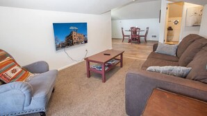 A living room with a sofa, armchair, and a coffee table. There is a dining table with chairs in the background. - Percival`s Perch at The Judge Jones Historic Homes (Flagstaff)