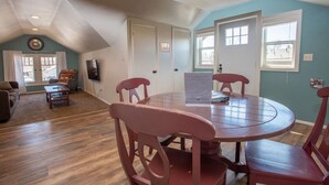 A dining area with a round table and four chairs, a sofa, and a television in a room with wooden flooring and blue walls. - Percival`s Perch at The Judge Jones Historic Homes (Flagstaff)