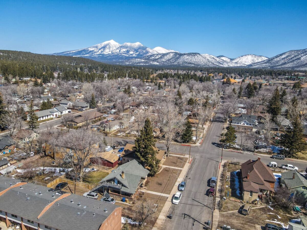 An aerial view of a residential area with houses, roads, and snow-capped mountains in the background.