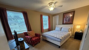 Quarto com cama, poltrona, escrivaninha e ventoinha no teto.