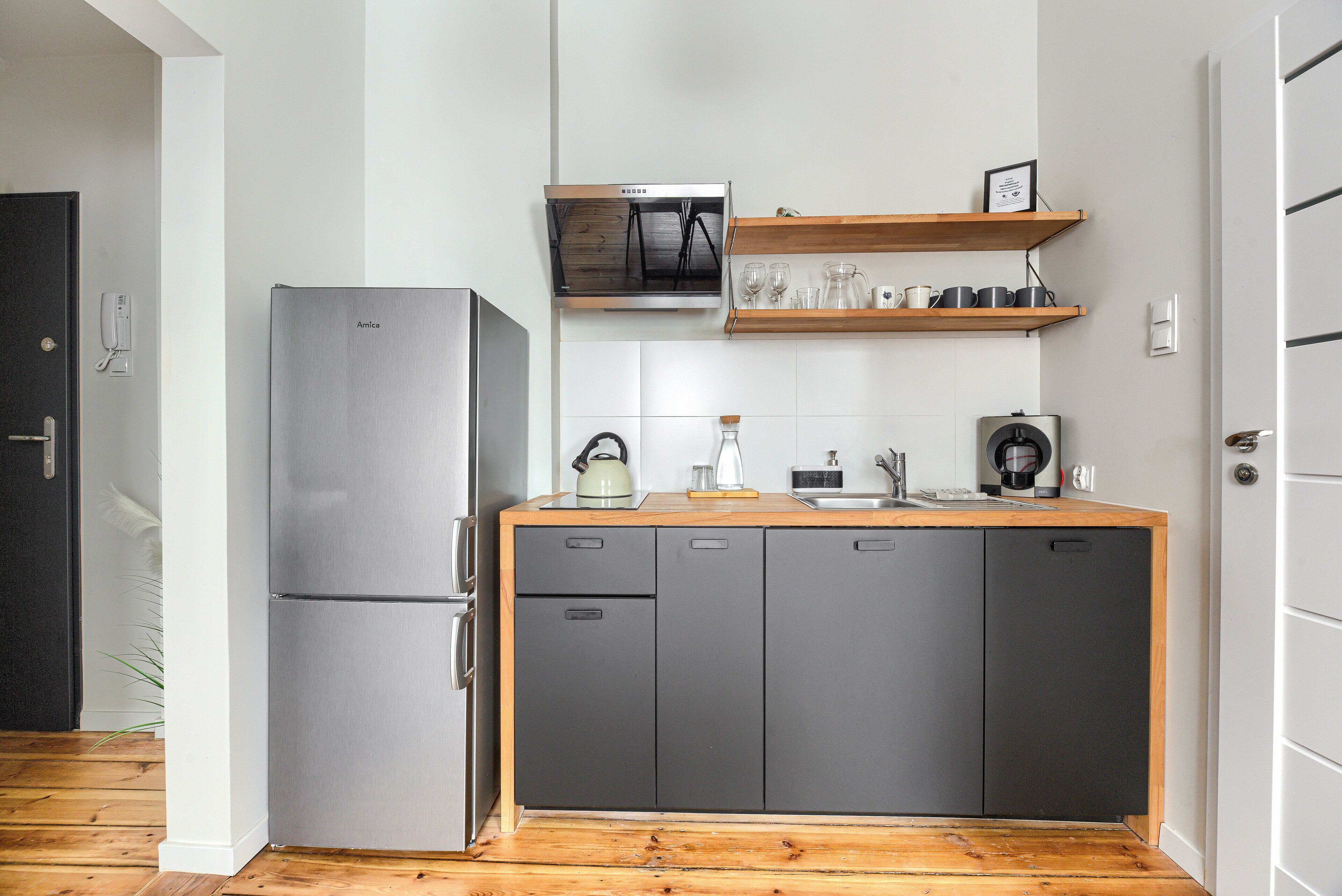 Una cucina compatta con frigorifero in acciaio inossidabile, forno a microonde e mensole in legno sopra il piano di lavoro.