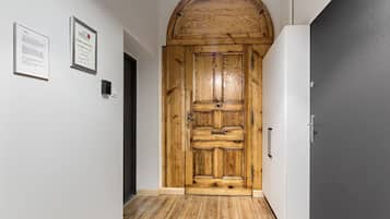 Una puerta de madera con diseño rústico, una pared blanca con diplomas enmarcados y una puerta gris a la derecha.