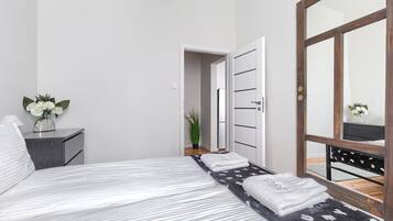 A modern bedroom with a bed, a nightstand, a mirror, and a door leading to another room.