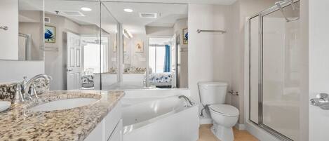 Un baño moderno con un espejo grande, encimera de granito, inodoro blanco y cabina de ducha de cristal.