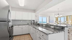 A modern kitchen with white cabinets, a granite countertop, and a stainless steel refrigerator. - Charming oceanfront resort w/indoor & outdoor pools, lazy river, kids pools-perfect for family trips (North Myrtle Beach)