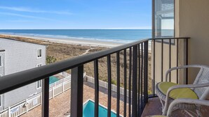 Un balcón con vista a la playa y al océano, una piscina y dos sillones de mimbre.