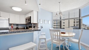 Una cocina moderna con armarios blancos, encimera de granito y comedor con mesa redonda y sillas blancas.