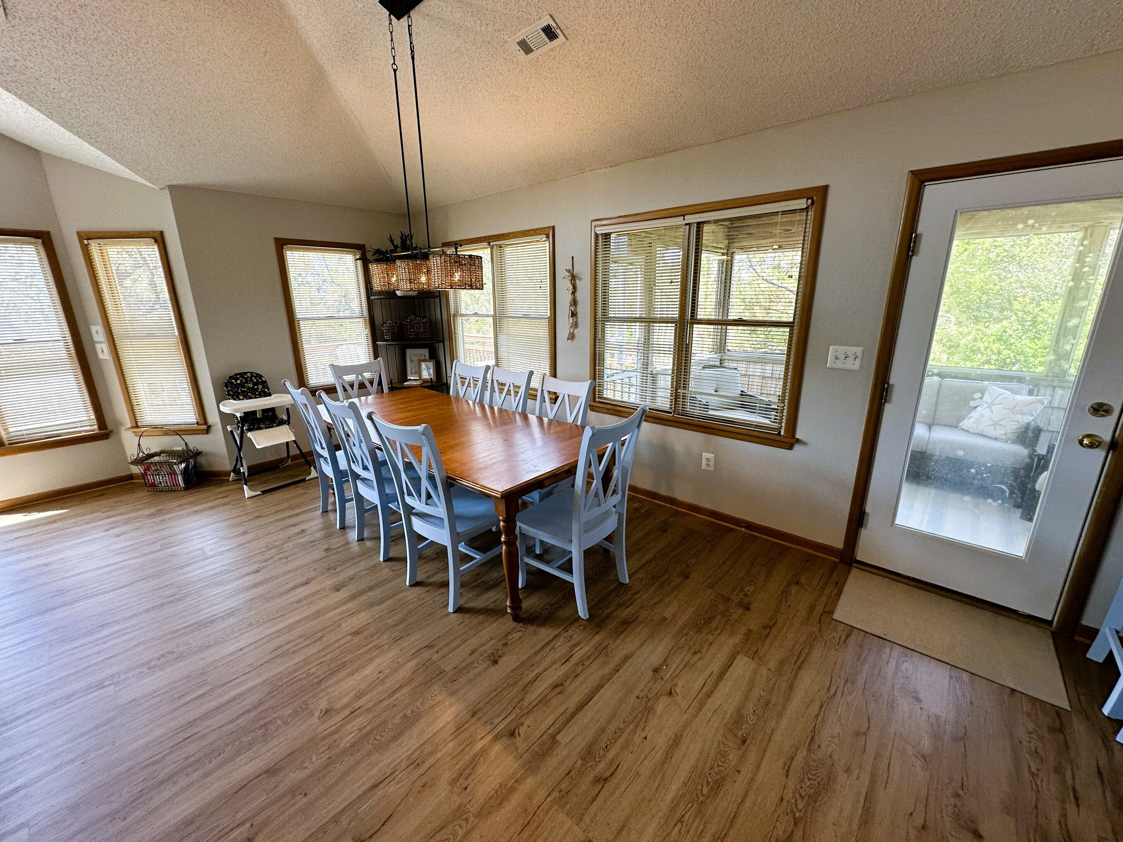Une salle à manger avec une table et des chaises en bois, de grandes fenêtres et une porte dotée d’un panneau en verre dépoli.