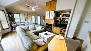 A modern living room with a sectional sofa, a coffee table, a lamp, a television, and a fireplace. - CP760- Crown Point Home with a Hot Tub and Oceanside! (Corolla)