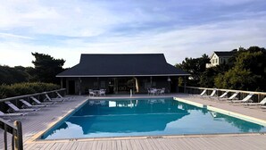 A rectangular swimming pool with a wooden deck, lounge chairs, and a covered seating area with tables and chairs. - CP760- Crown Point Home with a Hot Tub and Oceanside! (Corolla)