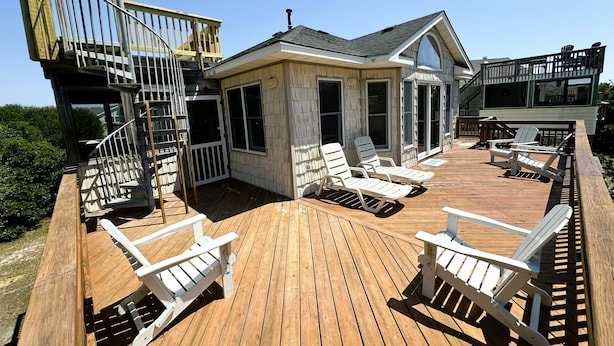 A wooden deck with lounge chairs and a staircase leading to a building with large windows. - CP760- Crown Point Home with a Hot Tub and Oceanside! (Corolla)