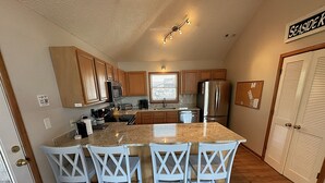 A kitchen with granite countertops, white chairs, wooden cabinets, stainless steel appliances, and a sign reading 'SEASIDE K.' - CP760- Crown Point Home with a Hot Tub and Oceanside! (Corolla)