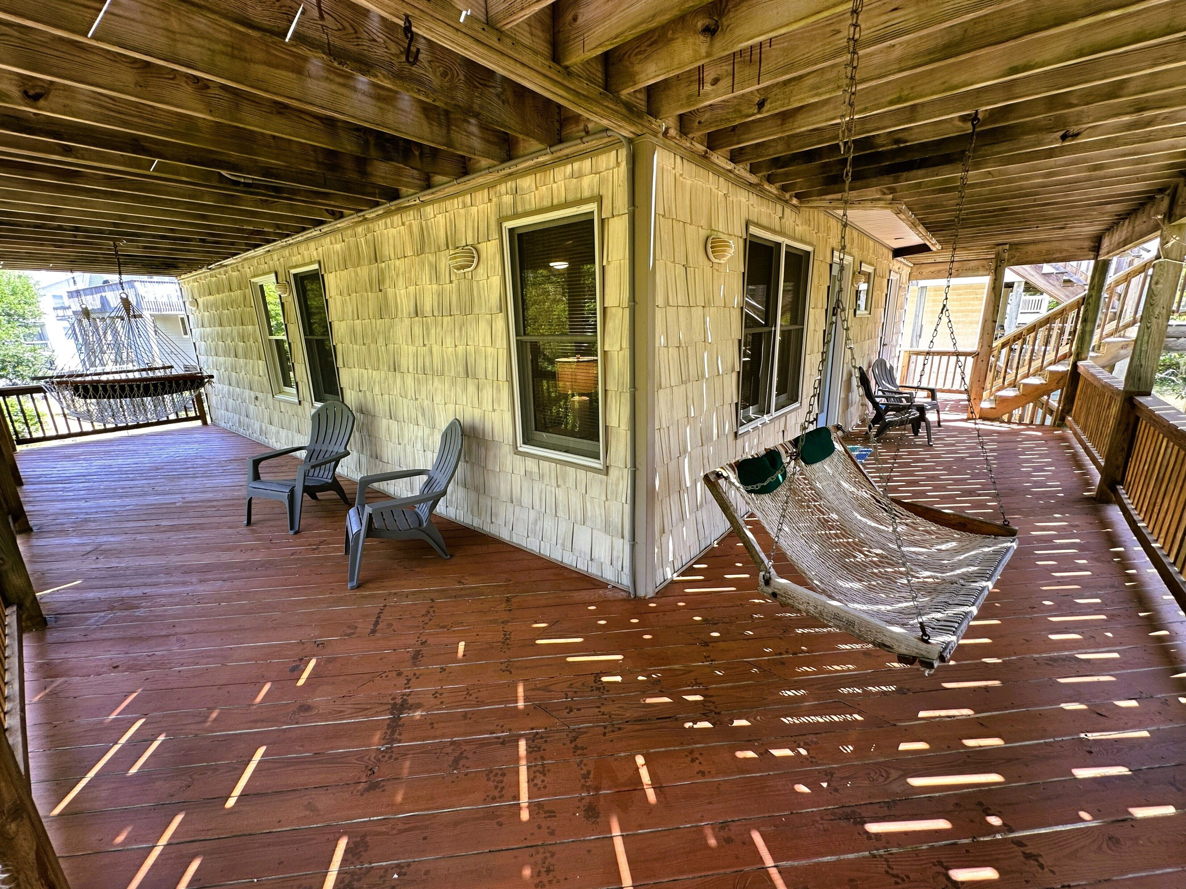 Een overdekt houten terras met Adirondack-stoelen, een hangmat en een houten gebouw met grote ramen.
