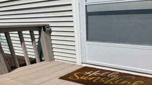 A wooden deck with a brown doormat that reads 'Hello Sunshine.'