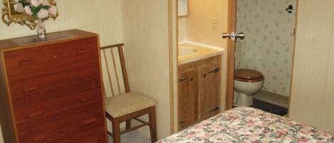 Een slaapkamer met een houten dressoir, een stoel, een bed met bloemenbeddels, een kaptafel met spiegel en een toilet.