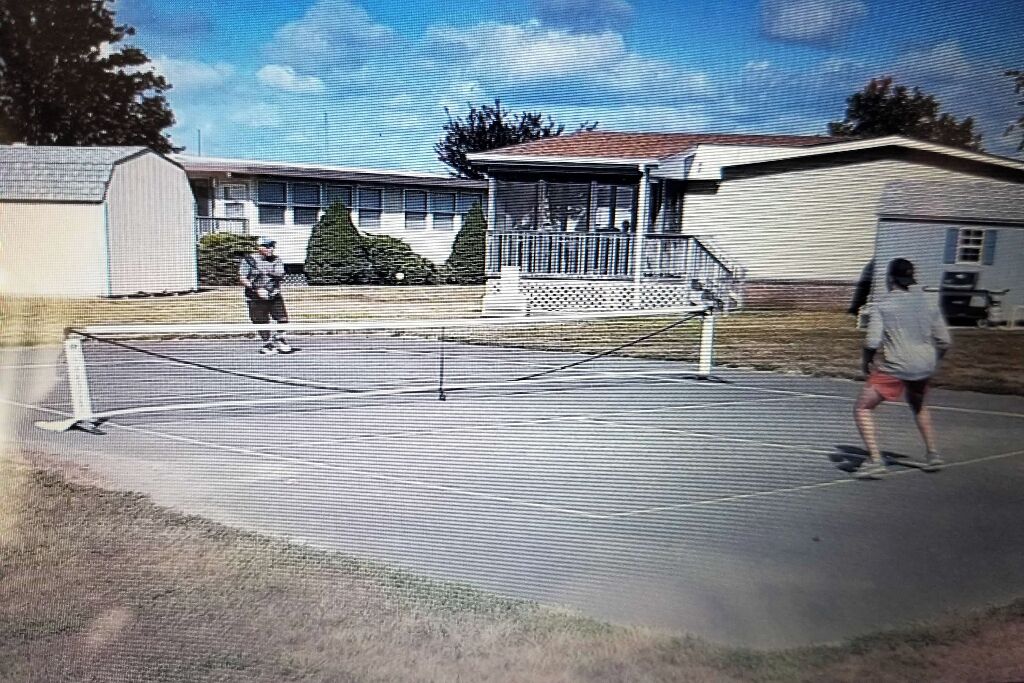 A tennis court with a net in the middle, surrounded by houses.