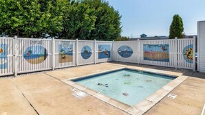 A swimming pool with a tiled deck, surrounded by a white fence with circular artwork.