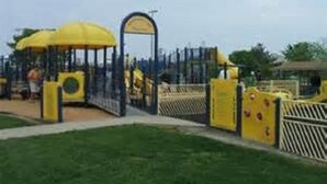 A playground with yellow play structures and a fenced area.