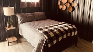 Un dormitorio con cama, mesita de noche, lámpara, ventana con cortinas y cestas tejidas en la pared.