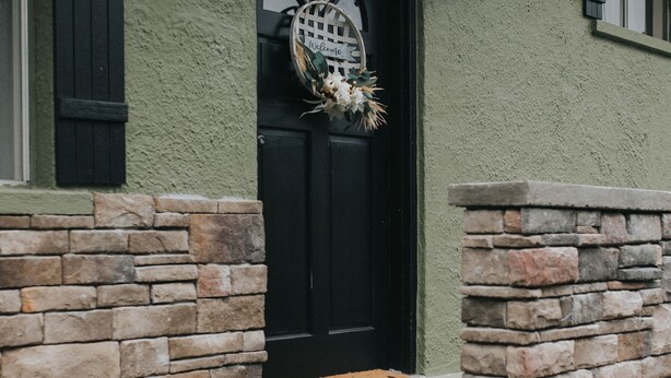 Una escalera de piedra que lleva a una puerta negra adornada con un adorno de bienvenida.