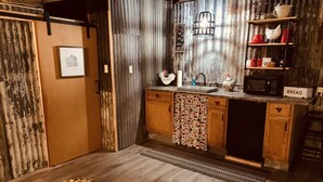 Una cocina rústica con armarios de madera, un lavabo y un microondas. Hay un cartel de 'WELCOME' sobre el lavabo y un cartel de 'BREAD' en la encimera.