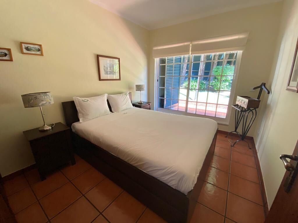 Een slaapkamer met een groot bed, een nachtkastje, een lamp en een raam met zonwering.
