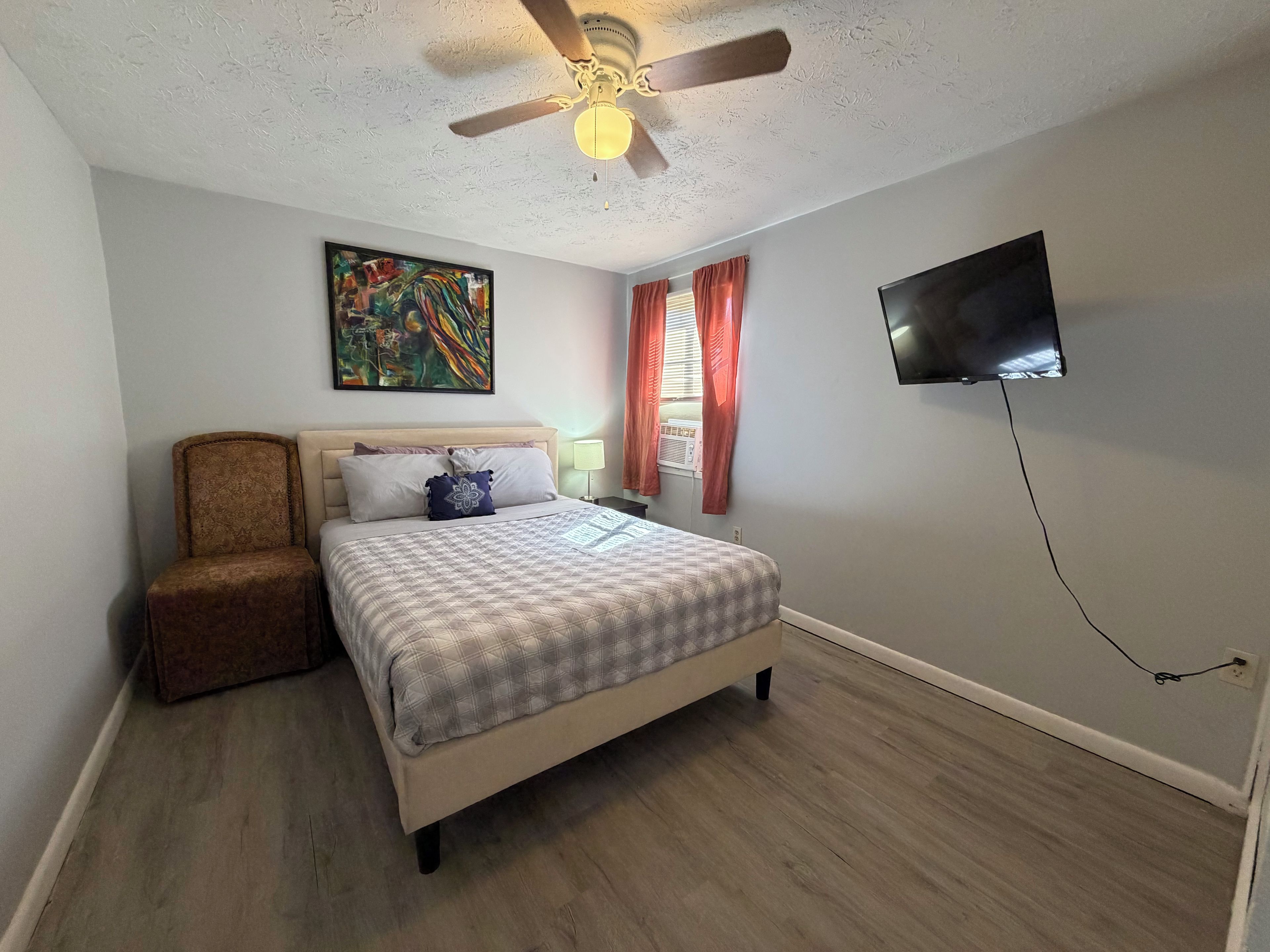 A bedroom with a bed, a ceiling fan, a TV, and a painting on the wall.