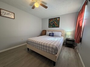 Une chambre à coucher avec un lit, un ventilateur de plafond, un tableau et une table de chevet avec une lampe.