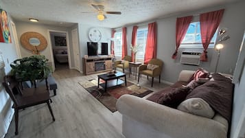 A living room with a sofa, chairs, a coffee table, a TV, and a ceiling fan.