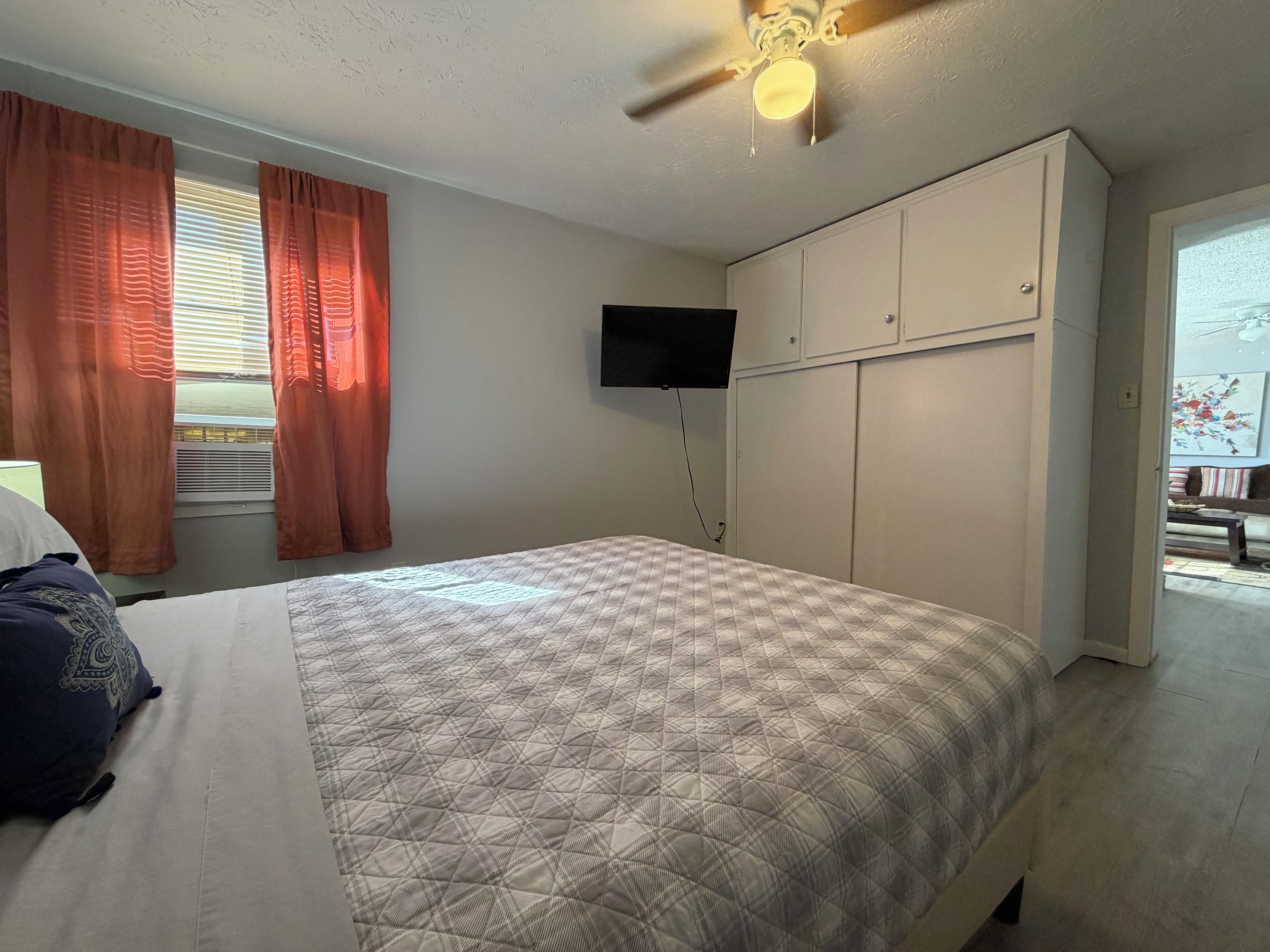 Ein Schlafzimmer mit einem Bett, einem Deckenventilator, einem an der Wand montierten Fernseher und einem Kleiderschrank.