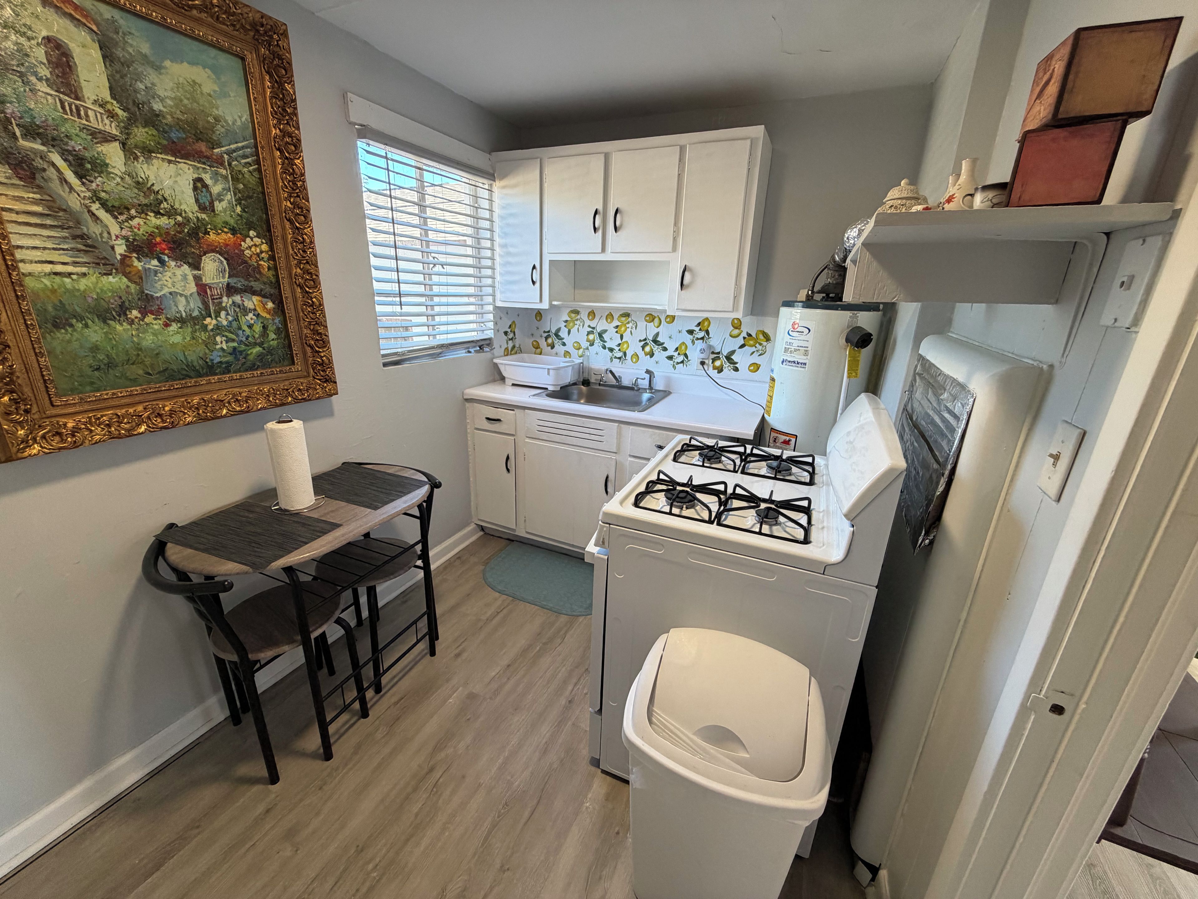 A compact kitchen with white cabinets, a gas stove, a sink, and a trash bin.