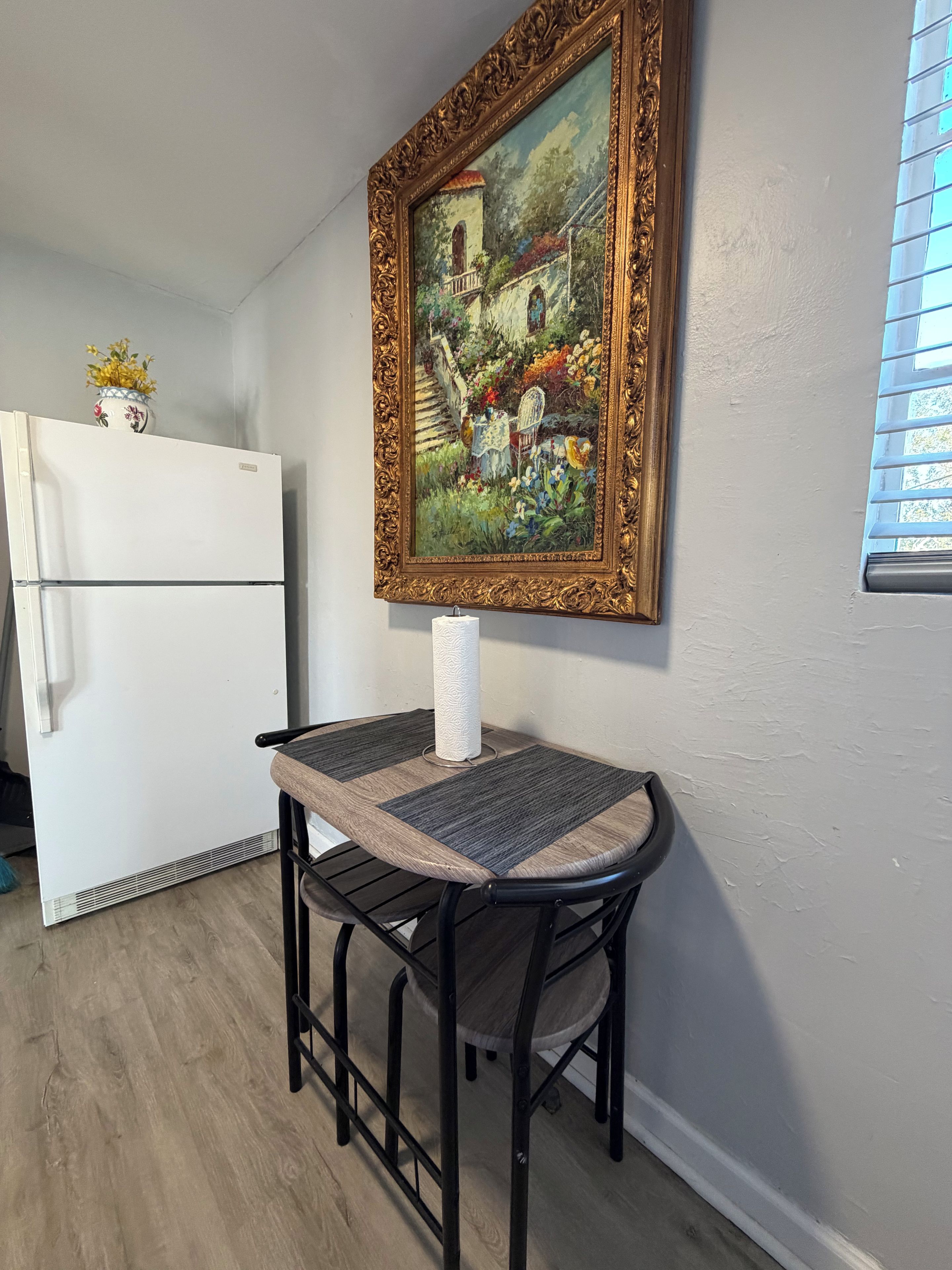 A dining area with a table and chairs, a white refrigerator, and a framed painting on the wall.
