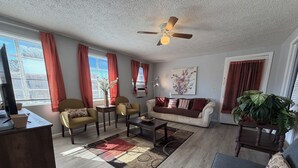 Un salon comprenant un canapé, des fauteuils, une table basse, un téléviseur et un ventilateur de plafond.