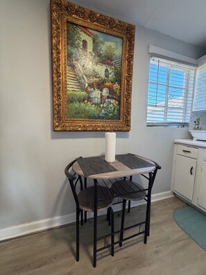 A dining area with a table and chairs, a painting on the wall, a window with blinds, and a white cabinet. - Historic Cozy Apartment near Hospital & VSU -SF (Valdosta)