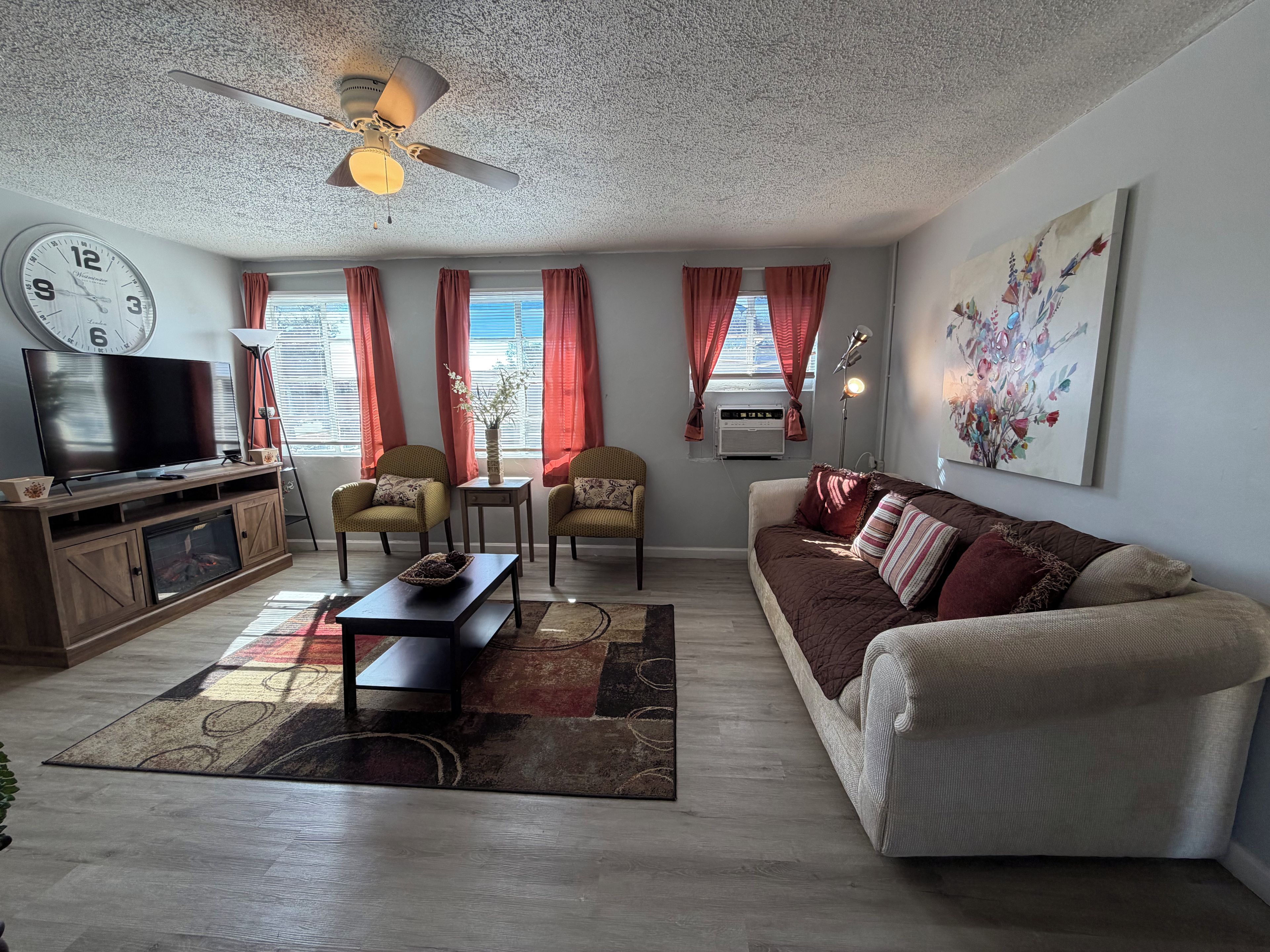 A living room with a television, sofa, chairs, a coffee table, and a ceiling fan.