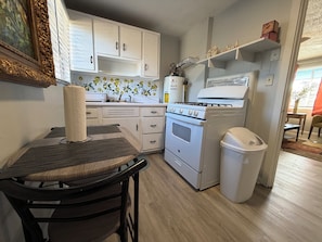 Una cocina funcional con muebles blancos, estufa y un cubo de basura.